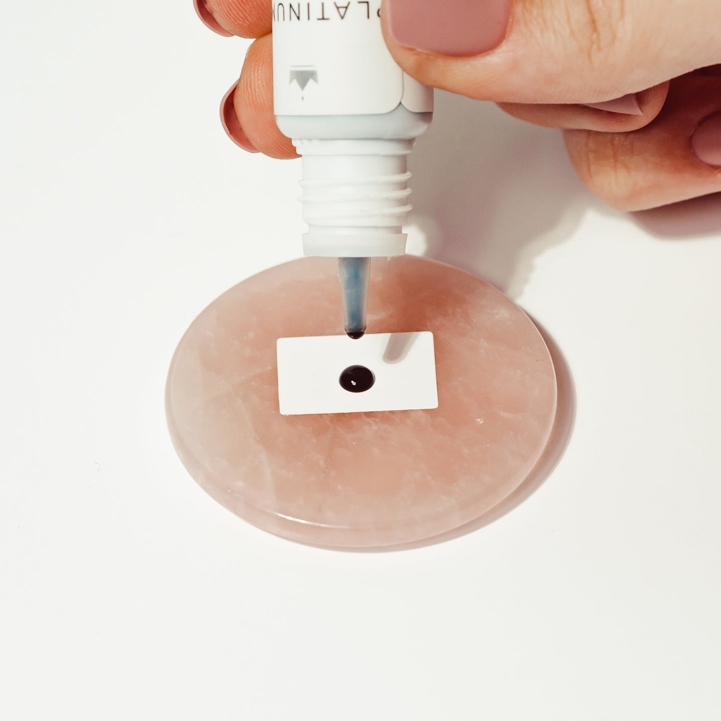 Platinum Plus adhesive bottle held in hands, dropping adhesive onto a jade stone with polystop adhesive preserver